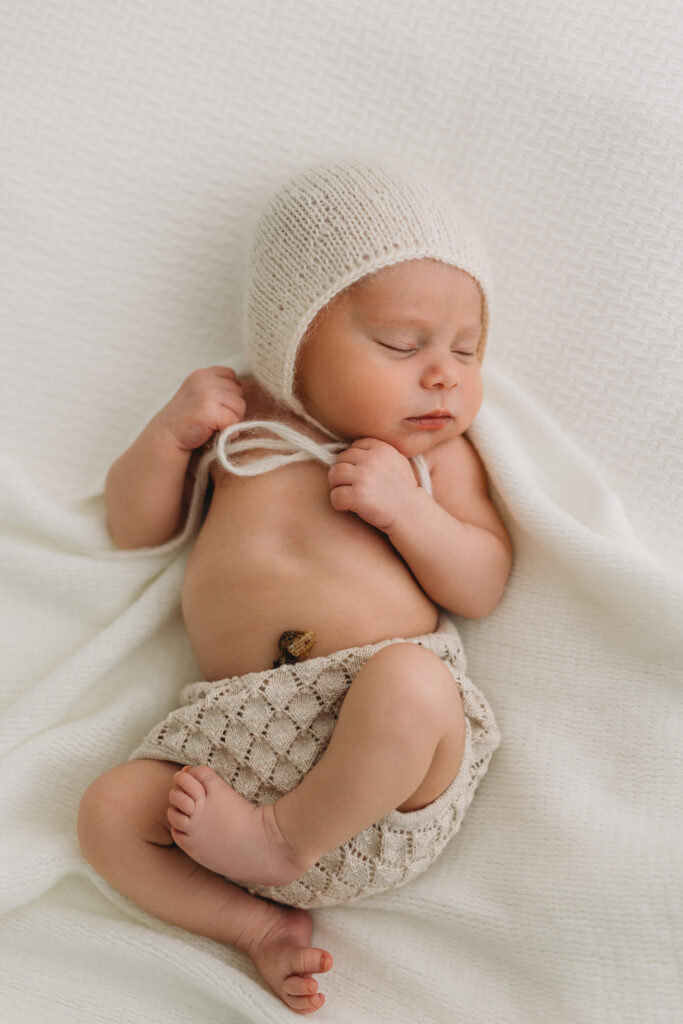 Newborn baby picture in Kelowna B.C. with baby wearing a bonnet and sleeping in neutral clothes and baby is 6 days old